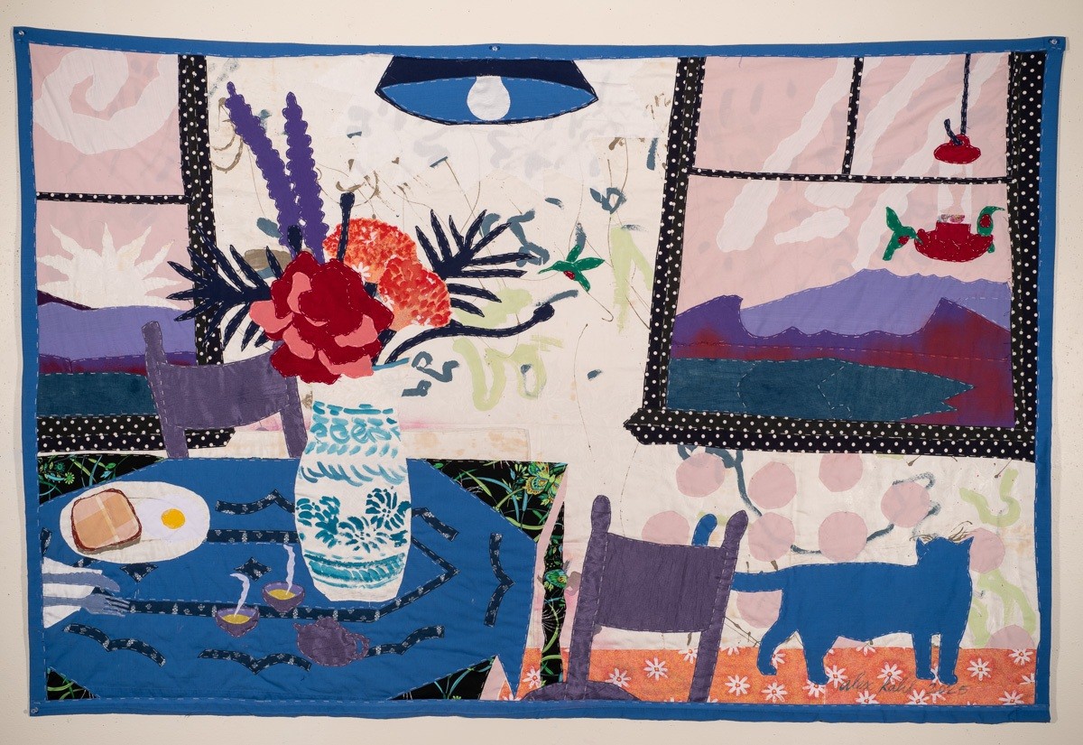Hand-quilted textile: Breakfast in bed — a blue table set with toast and a fried egg, a patterned vase of flowers, a cat, and windows onto a mountain lake.